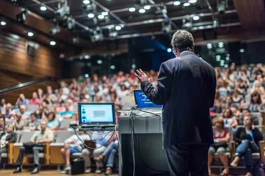 Speaker giving a talk on corporate business conference. Unrecognizable people in audience at conference hall. Business and Entrepreneurship event.