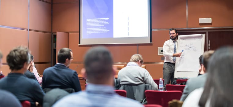 Public Speaker Giving a Talk at Business Meeting. Audience in the conference hall. Skilled coach asks questions to participants of business training. Business and Entrepreneurship concept.