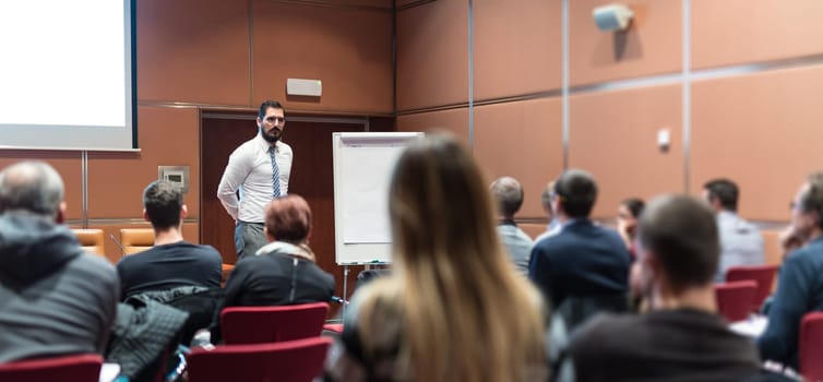 Public Speaker Giving a Talk at Business Meeting. Audience in the conference hall. Skilled coach answers questions of participants of business training. Business and Entrepreneurship concept.