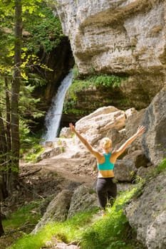 Active woman raising arms inhaling fresh air, feeling relaxed and free in beautiful natural environment under Pericnik waterfall in Vrata Valley in Triglav National Park in Julian Alps, Slovenia.