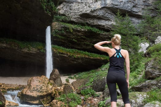 Active sporty woman in beautiful natural environment looking at Pericnik waterfall in Vrata Valley in Triglav National Park in Julian Alps, Slovenia.