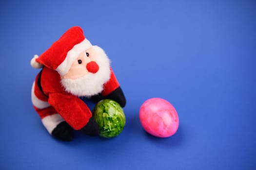 little santa claus with green and pink easter egg on blue ground