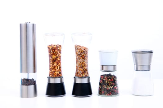 different spice mills with salt,pepper and other herbs in front of white background