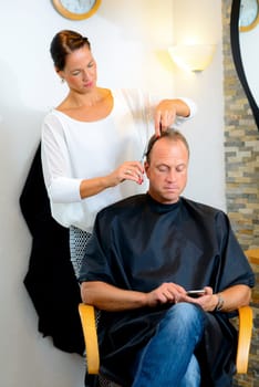 female hairdresser cutting hair of man in her shop