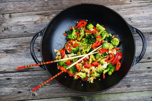 wok with colorful vegetables and chopsticks on wooden ground