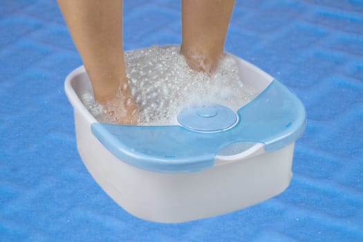 woman feet relax in foot bath in a vibrating foot massager on blue backround