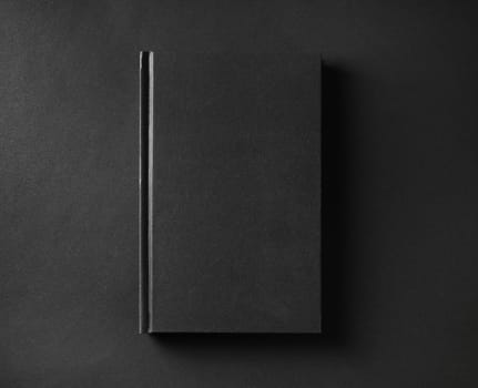 Photo of blank black book cover on black paper background. Flat lay.
