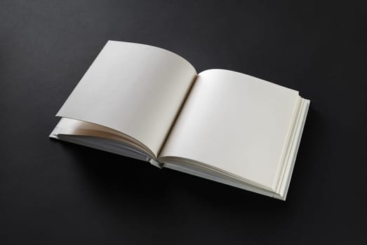 Open blank square book on black paper background.