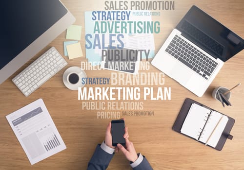 Businessman working at office desk, hands using a smart phone top view, marketing and business text concepts above desktop