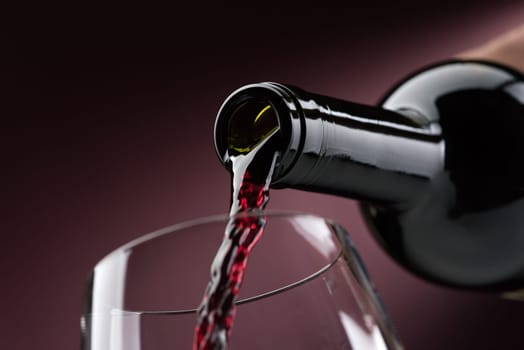 Pouring red wine from a bottle into a wineglass: wine tasting and celebration
