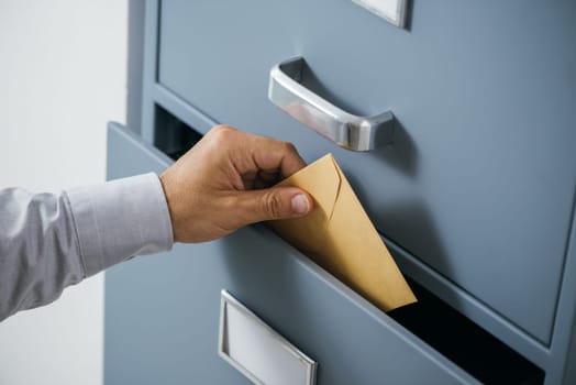 Businessman putting a closed envelope into a filing cabinet's drawer, data archive and protection concept