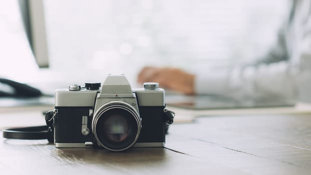Professional photographer working with a computer at the communication agency and vintage camera on the foreground