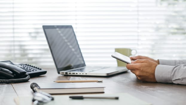 Businessman working at office desk, he is using apps on a digital tablet and connecting with a laptop