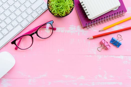 Top view office table with workspace and office accessories including calculator, mouse, keyboard, glasses, clips, flower, pen, pencil, note book, laptop and coffee on pink wooden background.