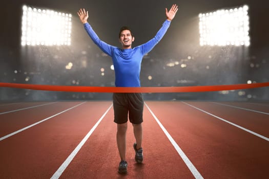 Happy asian athlete man running to finish line on the stadium