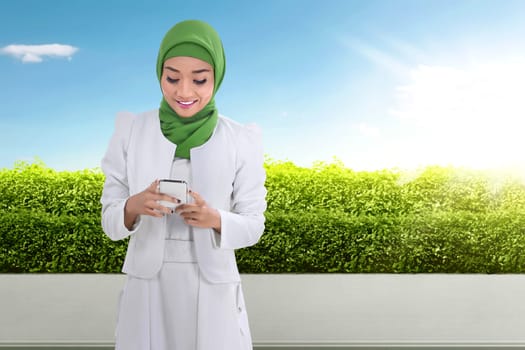Pretty asian muslim woman using cellphone on the park