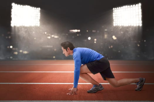 Handsome asian runner man in ready position to run on race track