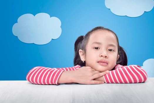 Joyful asian little girl relaxing on the table with blue decoration background