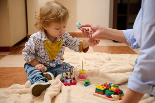 A young toddler engages in educational playtime with wooden toys, assisted by an adult, fostering learning and bonding moments. Ideal for concepts of childhood activities and parental care.