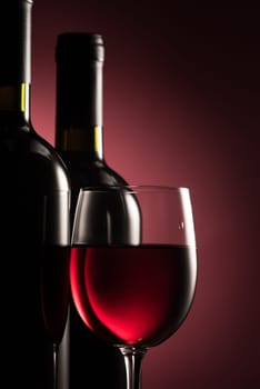 Selection on excellent red wine bottles and full wineglass on dark red background: wine tasting and celebration concept