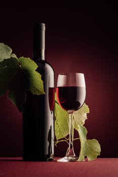 Red wine bottle, wineglass and vine branch still life