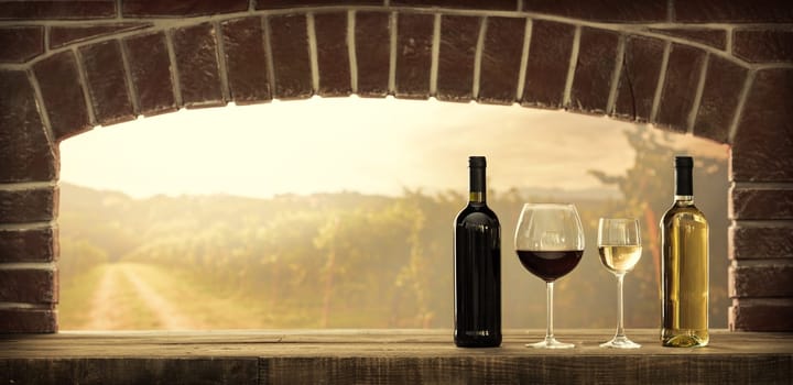 Wine tasting in the wine cellar: red and white wine bottles, wine glasses and panoramic view of the countryside vineyards at sunset