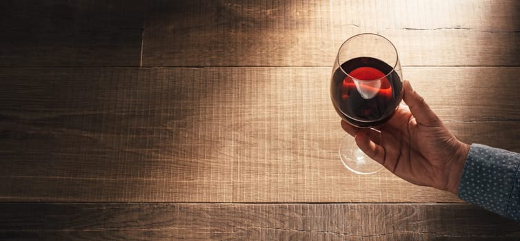 Man holding a balloon glass of delicious red wine on a rustic wooden table: wine tasting and celebration concept