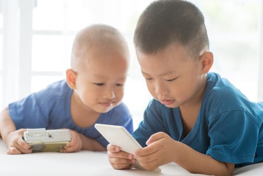 Young children addicted to technology gadget. Asian boys using smartphone at home.