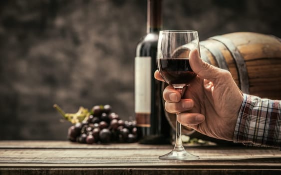 Senior wine maker tasting a glass of red wine in his cellar, wine bottle and wooden barrel on the background, wine tradition and culture concept