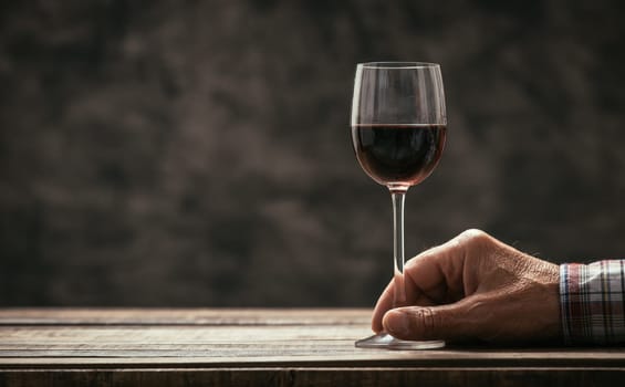 Senior man and wine expert tasting a glass of red wine in the cellar, hand close up, wine tradition and culture concept