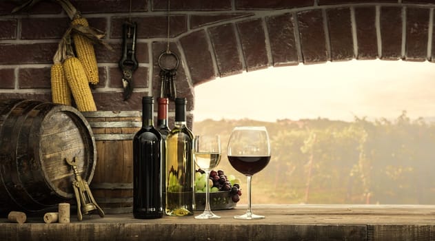 Wine bottles, wineglasses, barrels next to the cellar window and beautiful panoramic view of countryside vineyards: winemaking and wine culture concept