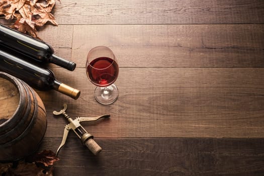 Excellent red wine bottles, wineglass, barrel and corkscrew on a rustic wooden table: traditional winemaking and wine tasting concept