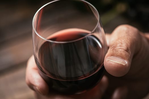 Senior man tasting a glass of italian red wine, rustic wooden table on the background, hand close up