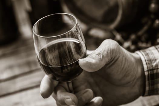 Senior man tasting a glass of italian red wine, rustic wooden table on the background, hand close up