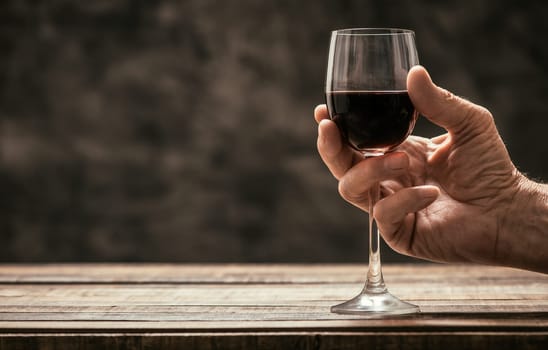 Senior wine expert tasting a glass of red wine in the cellar, hand close up, wine tradition and culture concept
