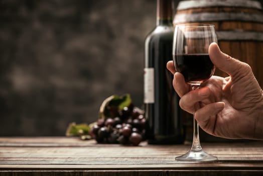 Senior man drinking a glass of expensive red wine in his cellar, wine bottle, grape and barrel on the background, wine tradition and culture concept