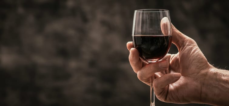 Senior wine expert tasting a glass of red wine in the cellar, hand close up, wine tradition and culture concept