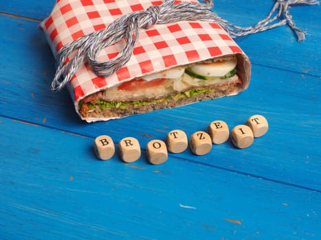 Tasty whole grain sandwich on a blue kitchen table, wooden dices with the German words Breakfast, healthy eating cocnept