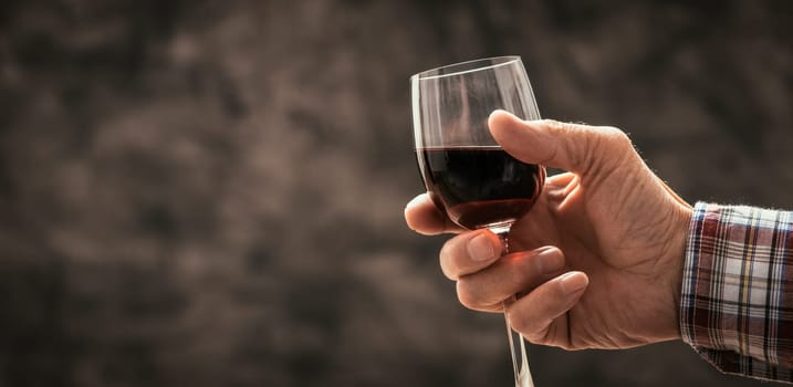 Senior man and wine expert tasting a glass of red wine in the cellar, hand close up, wine tradition and culture concept