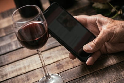 Man tasting a glass of red wine and using apps on his smartphone, wine culture and technology concept