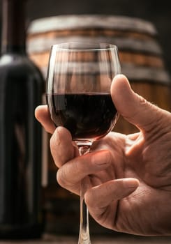 Senior man drinking a glass of expensive red wine in his cellar, wine bottle and barrel on the background, wine tradition and culture concept