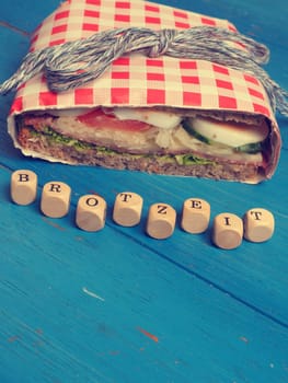 Tasty whole grain sandwich on a blue kitchen table, wooden dices with the German word Breakfast, healthy eating concept, vintage color stylized