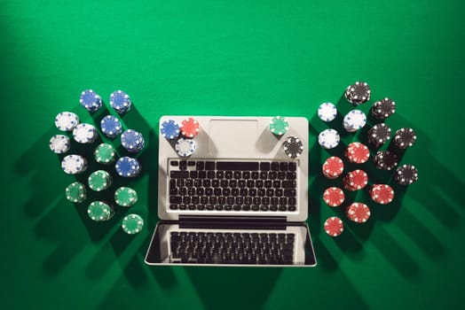 Poker and casino online gaming concept with laptop and stacks of chips on green table, top view