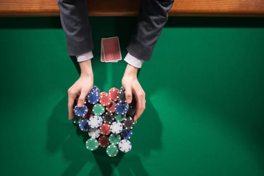 Poker player betting all in and holding a lot of chips stacks, hands close up, top view