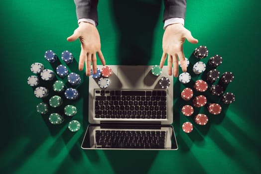 Online player's hands palms up with laptop and stack of chips all around on green table top view