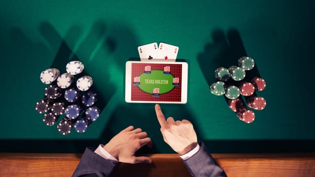 Poker player's hands with digital tablet, stacks of chips and cards on green table, top view