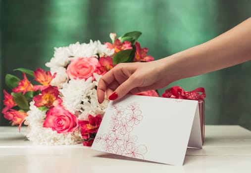 Love background with pink roses, flowers, gift, card on table. Concept of holiday Mother's Day. Copy space. Female hand at colorful studio background. holiday congratulations. Mother and love. Postcard