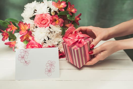 Love background with pink roses, flowers, gift, card on table. Concept of holiday Mother's Day. Copy space. Female hand at colorful studio background. holiday congratulations. Mother and love. Postcard