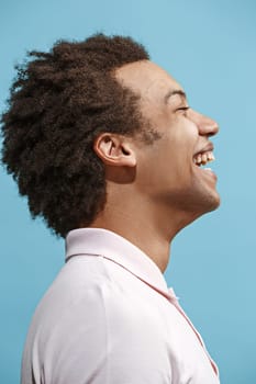 Happy afro business man standing and smiling isolated on blue studio background. Beautiful male half-length portrait. Young emotional man. The human emotions, facial expression concept. Profile view.