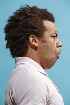 Argue, arguing concept. Beautiful male half-length portrait isolated on blue studio backgroud. Young emotional surprised afro man Human emotions, facial expression concept. Profile view